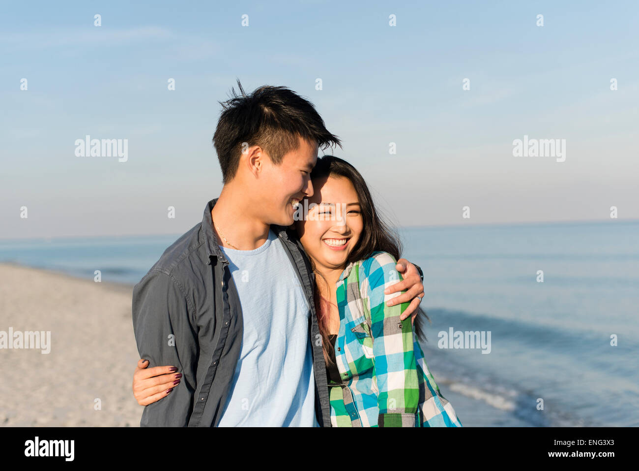 Smiling Korean couple hugging on beach Stock Photo