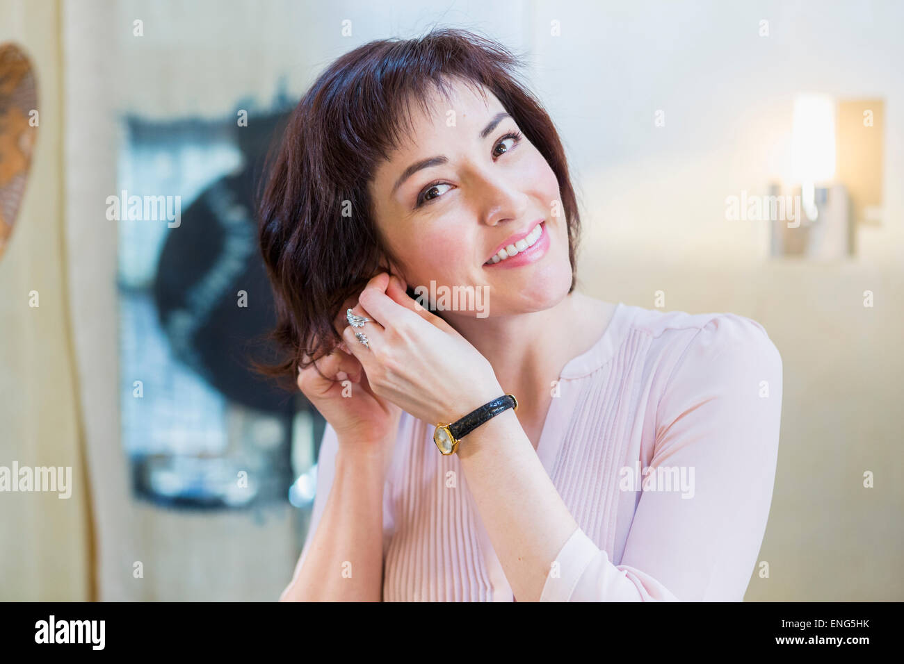 Hispanic woman putting on earrings in mirror Stock Photo