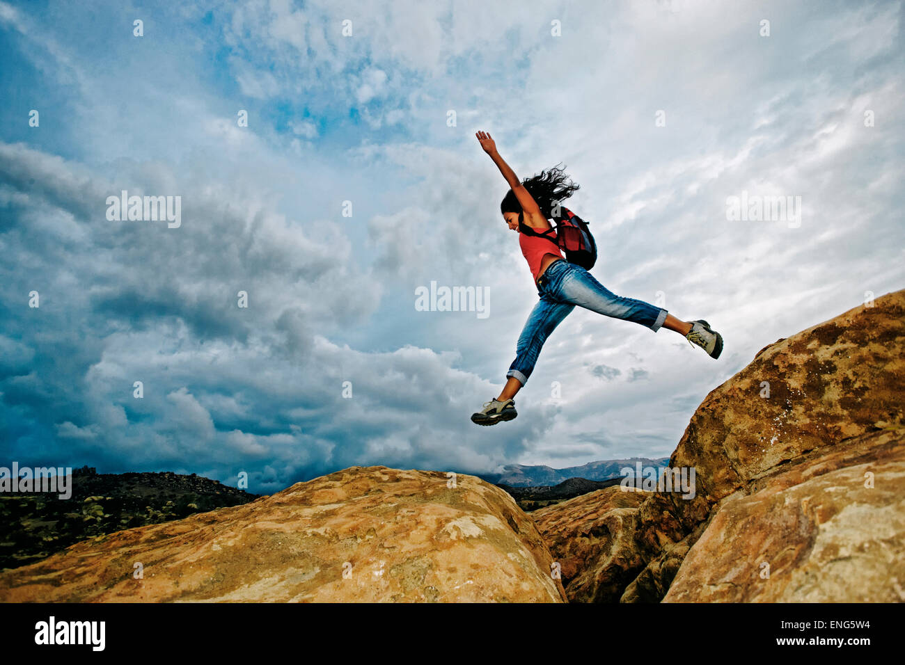 Hispanic woman jumping crevasse on rock formation Stock Photo