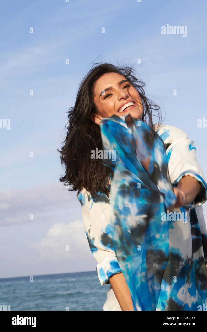 Hispanic woman playing with blue fabric on beach Stock Photo