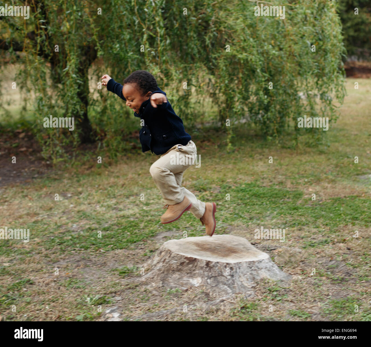 African American boy playing on stump in park Stock Photo