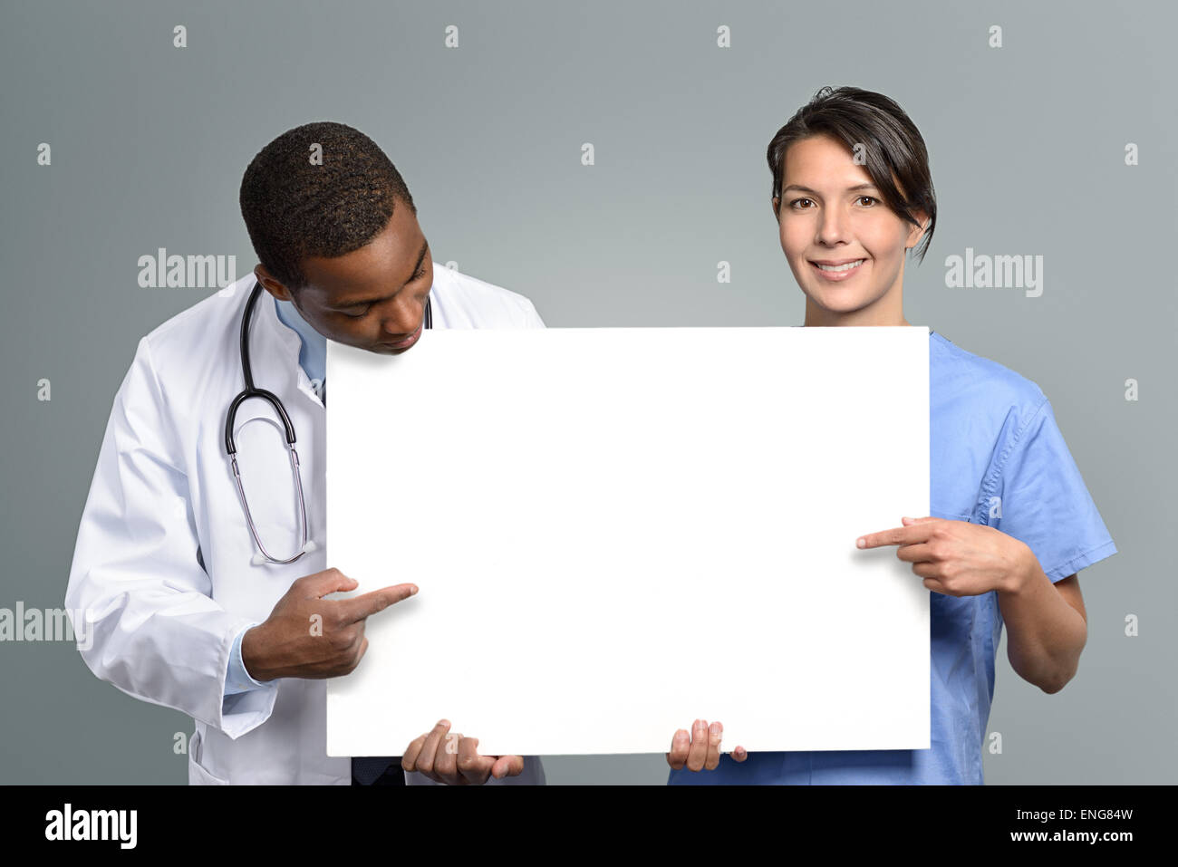 Multiethnic medical team of an African doctor in a lab coat and stethoscope and a nurse in scrubs holding a blank white sign Stock Photo
