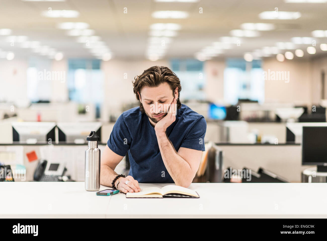 A man leaning on his elbow and looking at an open book on an office