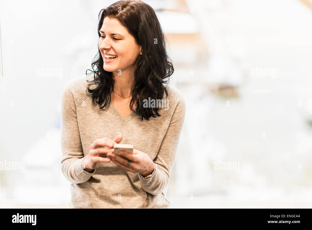 A business woman seated by a window using her smart phone. Stock Photo