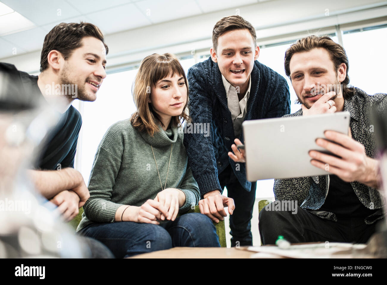 Four people, colleagues at a meeting, and one man sharing a tablet with the group. Stock Photo