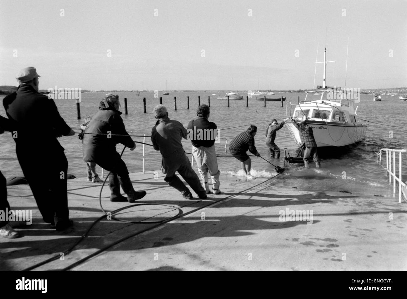 team of people pull together to haul a pleasure boat out of the sea and onto dry land Stock Photo