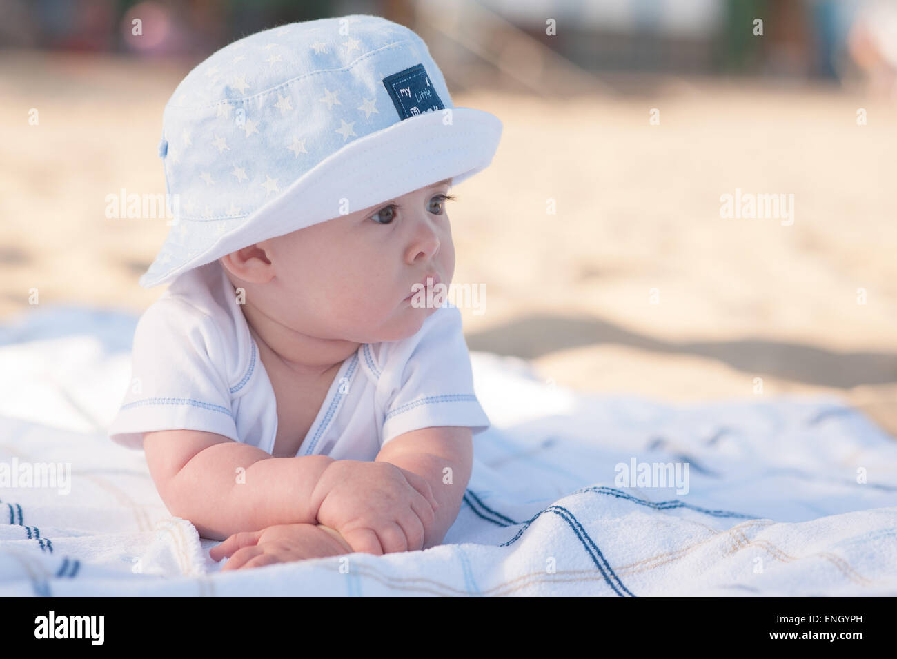 6 month old baby boy in sun hat laying on a blanket on the beach resting  his weight on his arms Stock Photo - Alamy