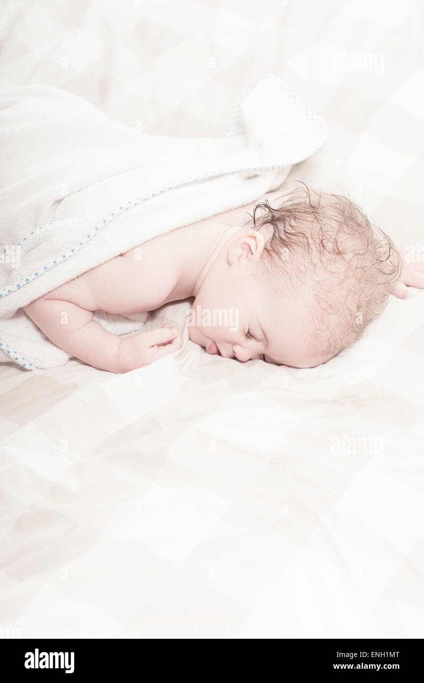 Curly haired Caucasian toddler boy asleep on bed with wet hair after a bath Stock Photo