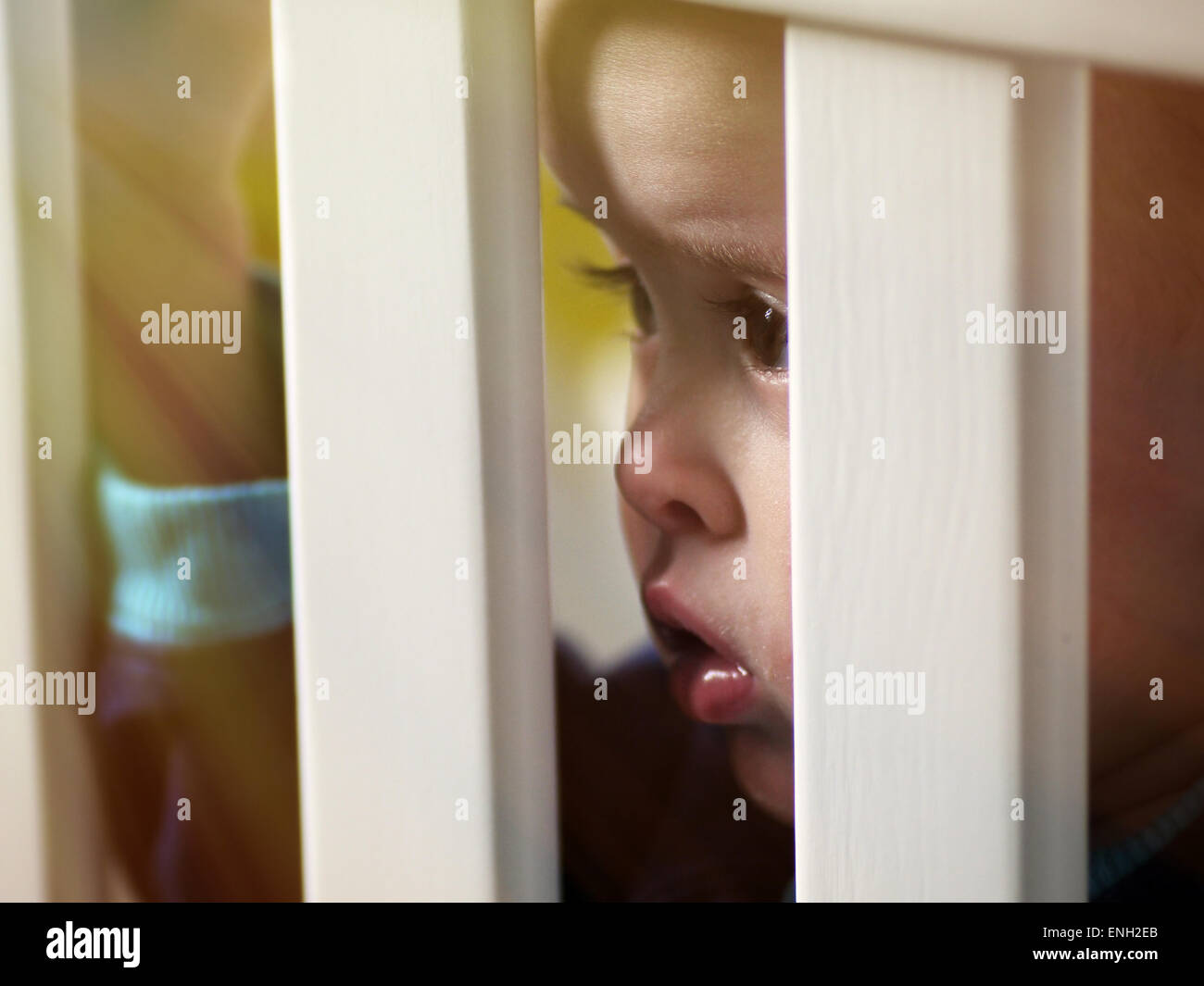 Baby boy peering through cot bars Stock Photo