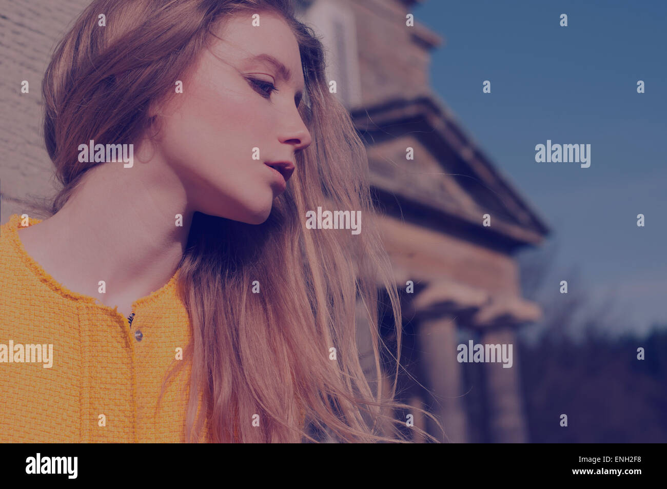 Blue toned vintage style portrait of young woman with windswept blonde hair outside an old building Stock Photo