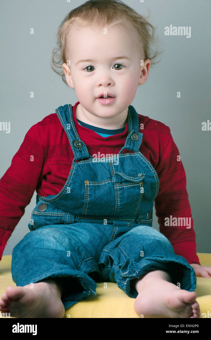 Portrait of smiling one year old baby boy in red top and dungarees Stock Photo
