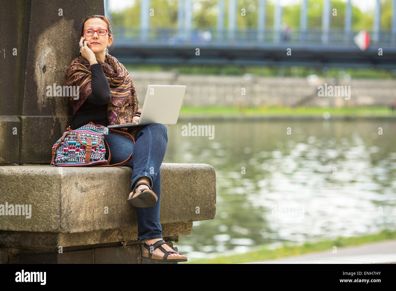Young woman with laptop talking on the phone, outdoors in the city. Stock Photo