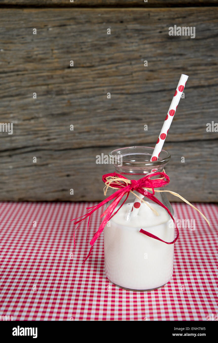 Polka dot straw in white milk with old-fashioned milk bottle and raffia bow on gingham. Stock Photo