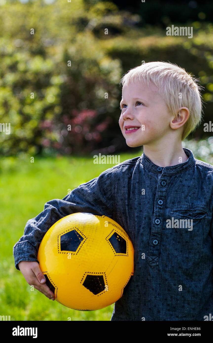 Preschool Child with Football, soccer ball. Boy that's out in the garden with his football . His football is yellow. He wears a Stock Photo