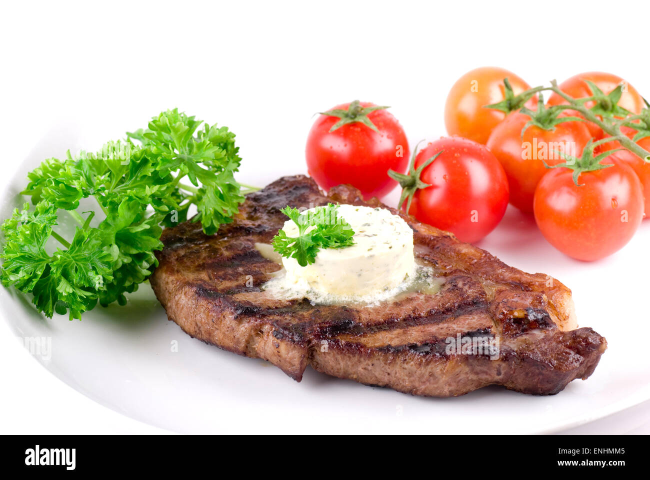 Strip steak with parsley butter on a white plate. Parsley and tomatoes garnish. Stock Photo
