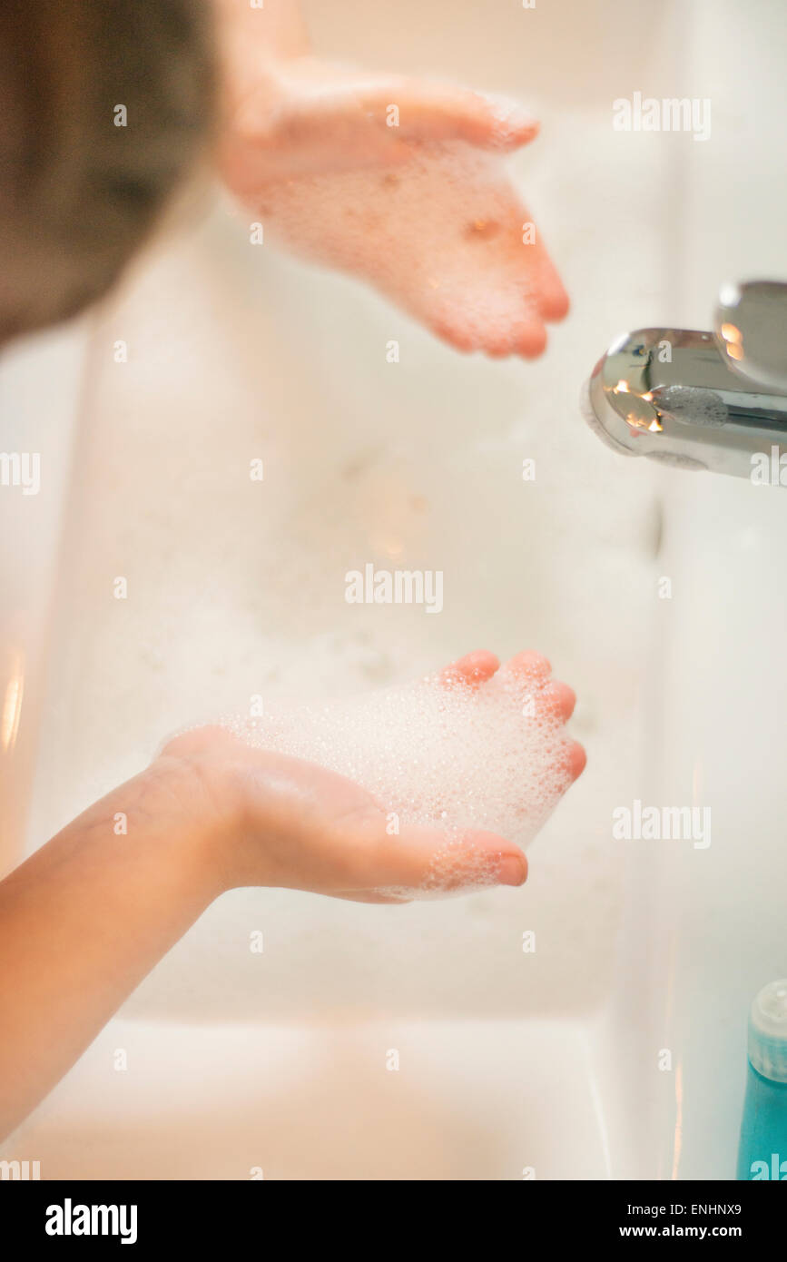 Little girl washing hands in bathroom sink filled with soap suds. Stock Photo