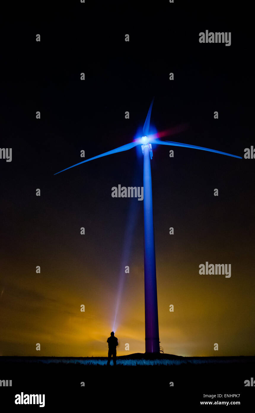 The wind turbine at night in an unusual light- a lonely man shines screw with flashlight . The concept of eco-friendly produce Stock Photo