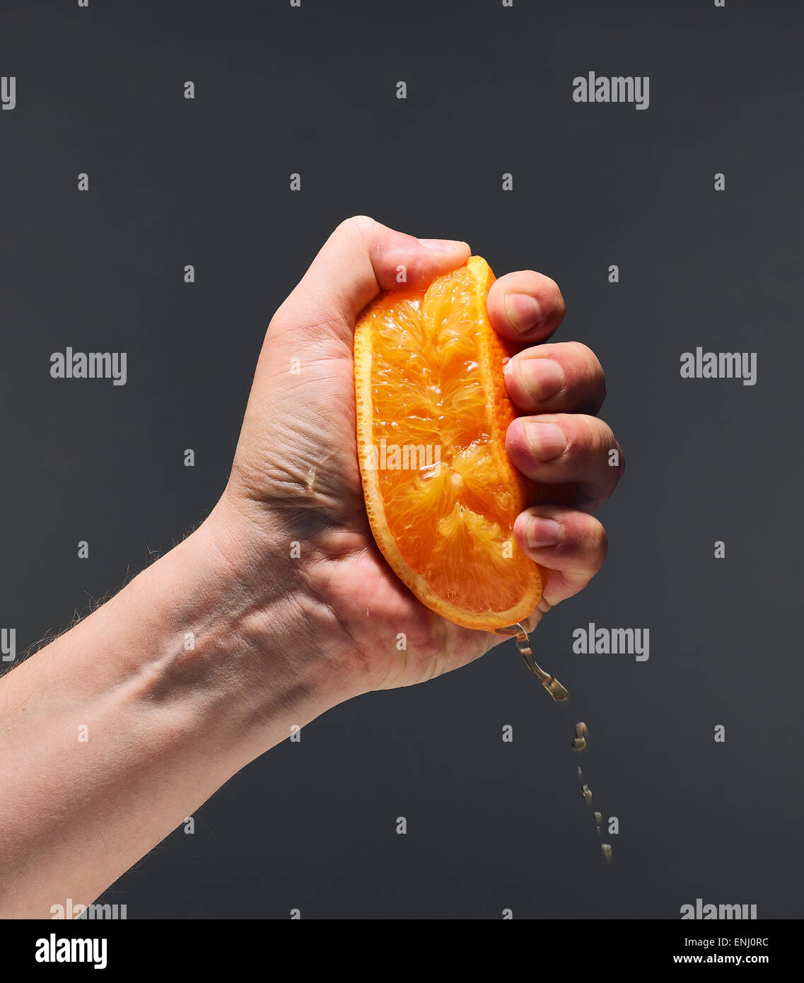 Male hand squeezing juicy orange, dark background Stock Photo