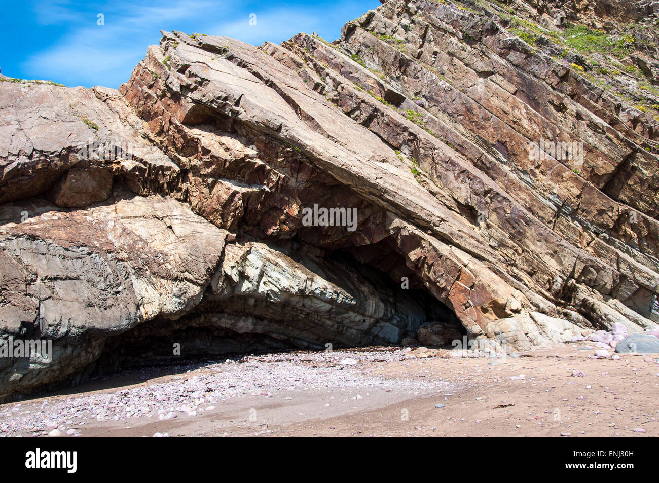 Rocks at one end of Marloes sands in Pembrokeshire. Sloping strata in the warm coloured cliffs. Stock Photo