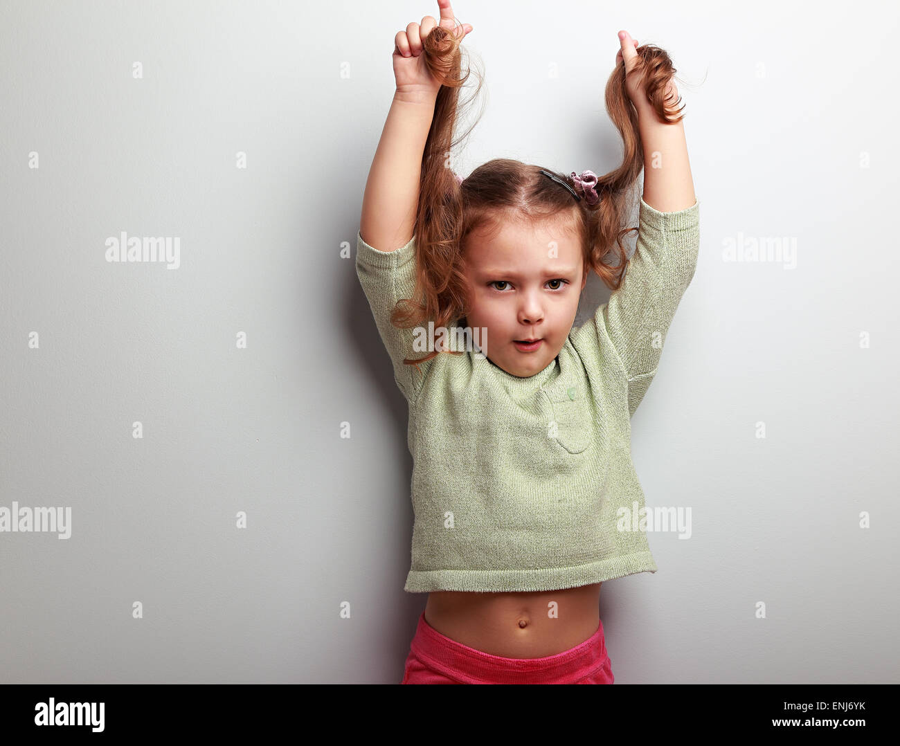 Active Unhappy Kid Girl Pulling Her Long Hair On Blue Wall