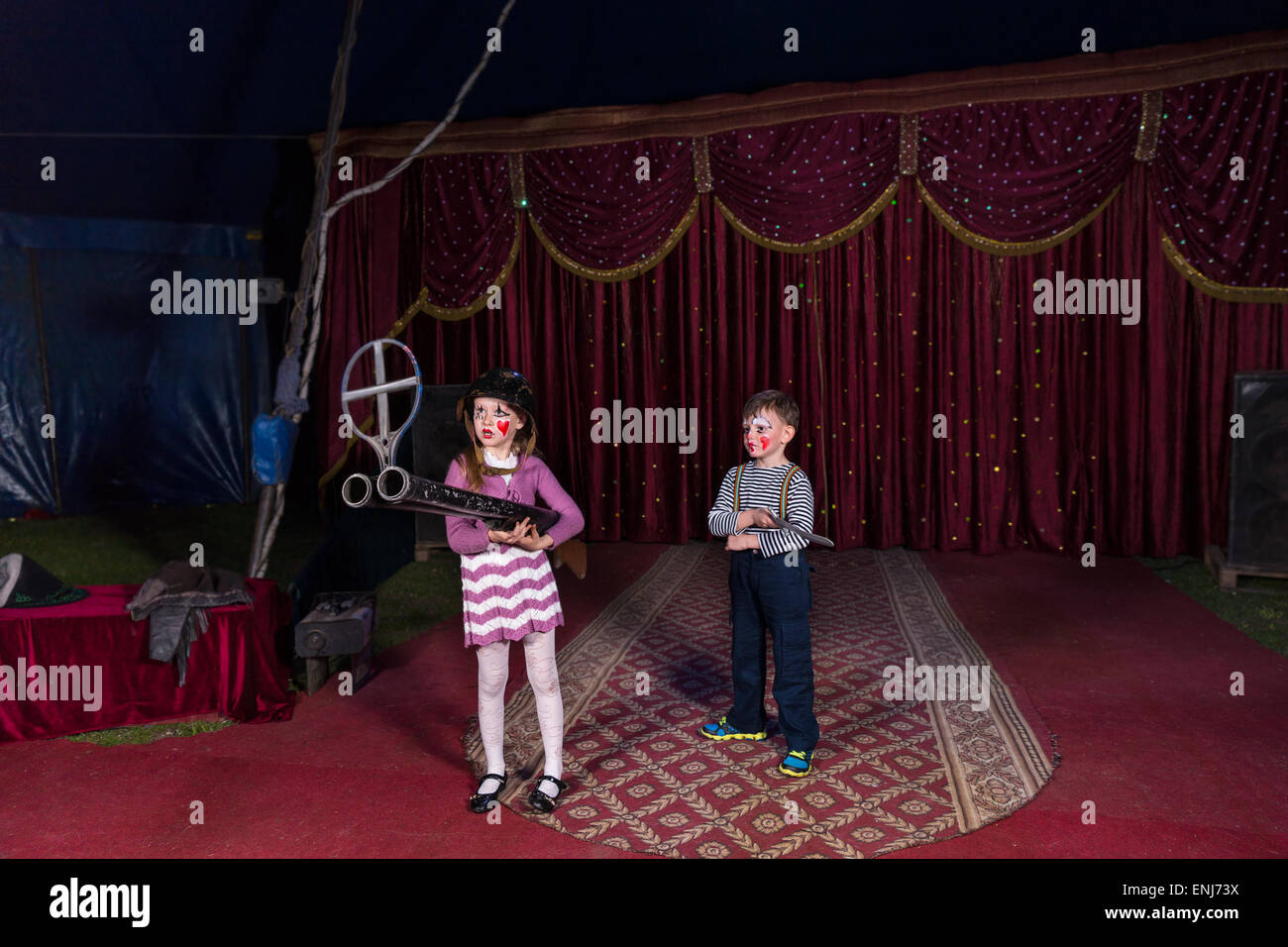 Boy and Girl Dressed as Clowns Standing on Stage Holding Large Double Barreled Shot Gun Stock Photo