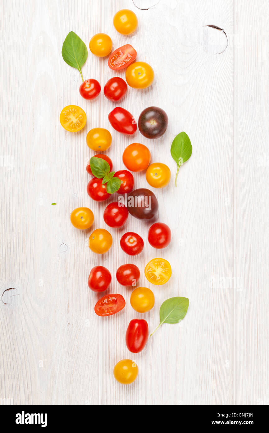 Colorful cherry tomatoes and basil on wooden table background. Top view ...