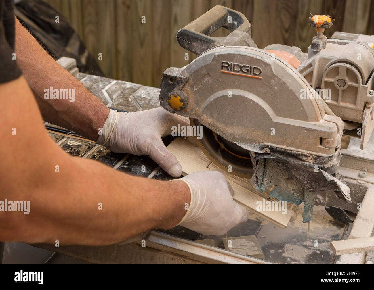 ARLINGTON, VIRGINIA, USA - Worker wearing latex gloves cuts ceramic tiles with a wet tile saw. Stock Photo