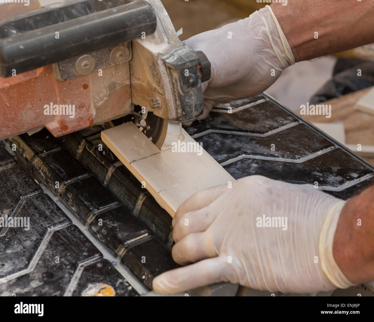 ARLINGTON, VIRGINIA, USA - Worker wearing latex gloves cuts ceramic tiles with a wet tile saw. Stock Photo