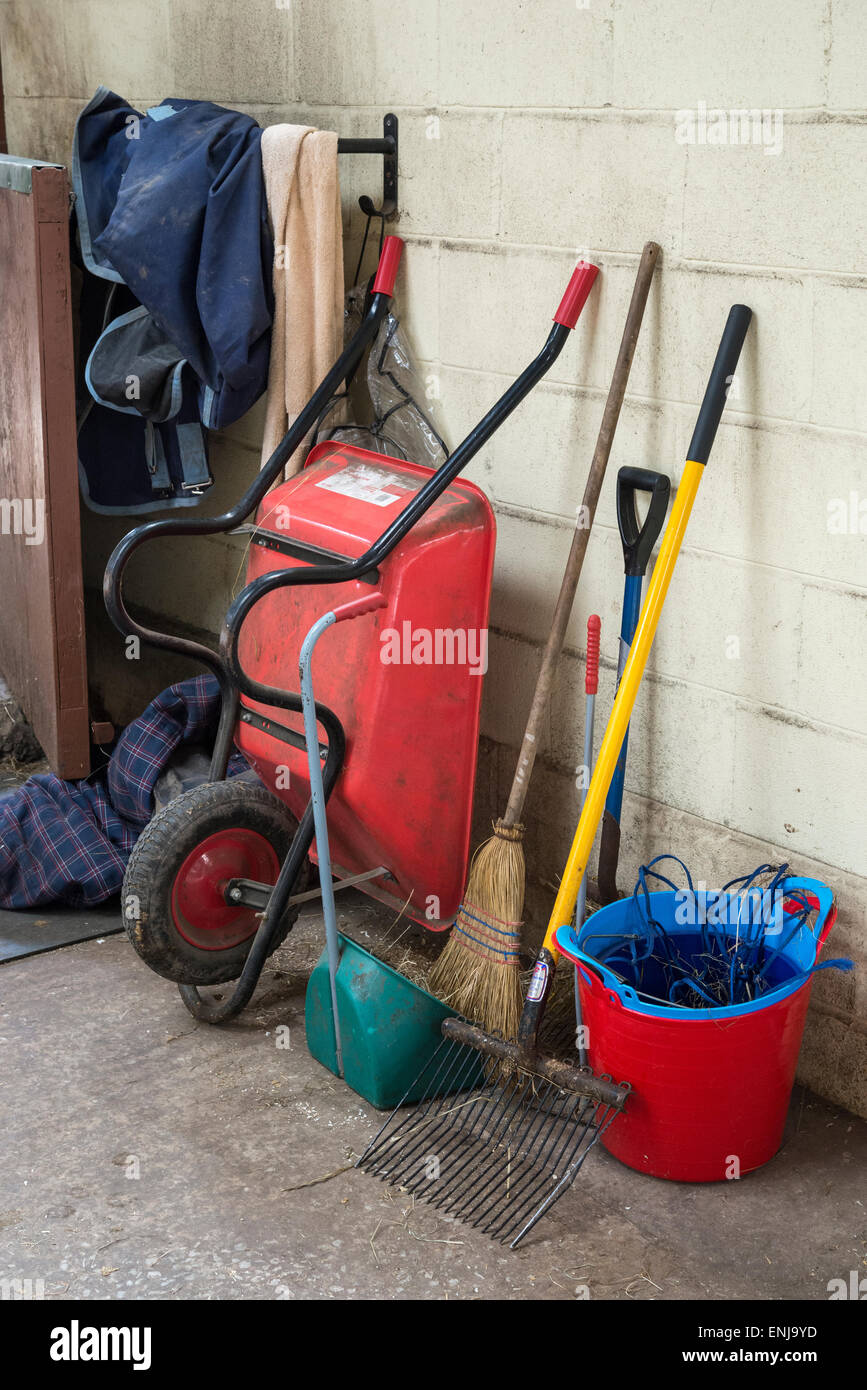 Wheelbarrow and other tools in an equestrian stable yard. Buckets, brushes, rugs and mucking out fork. Stock Photo