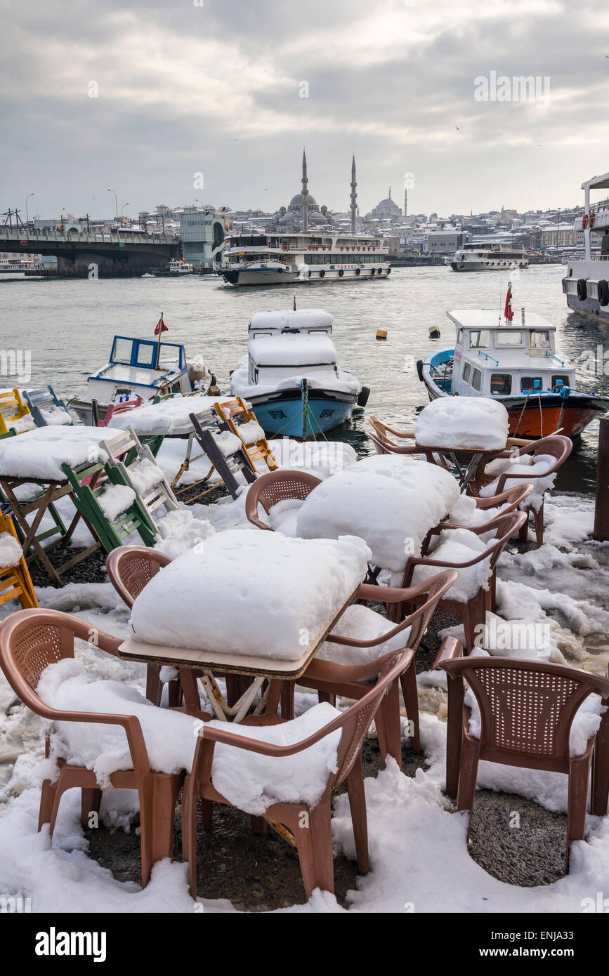 Snow covered cafe chairs on Karakoy waterfront, looking across the Golden Horn toward the Yeni mosque at Eminonu  and the Istanb Stock Photo