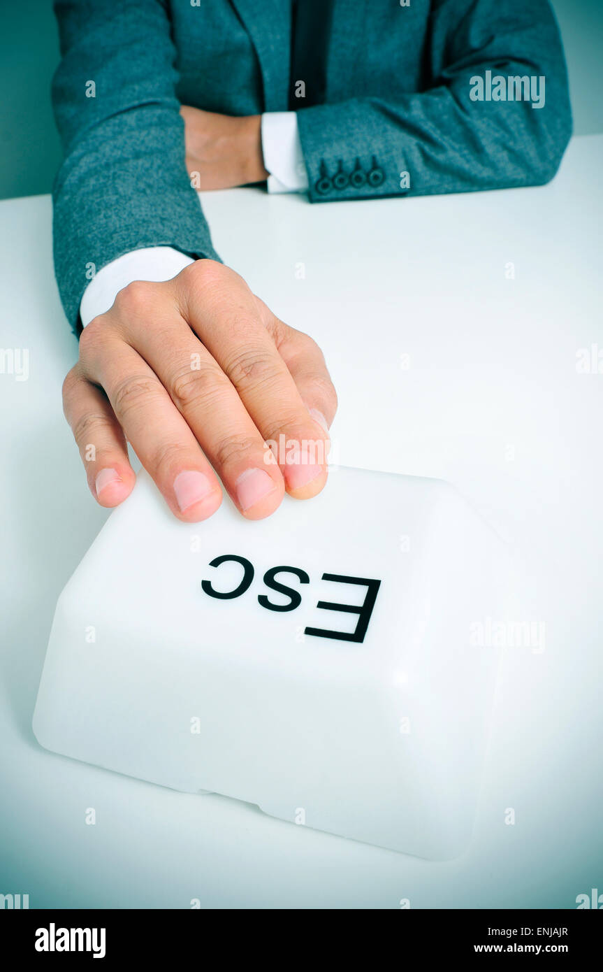 young caucasian man wearing a gray suit sitting at his office desk pressing a giant escape key with his hand Stock Photo