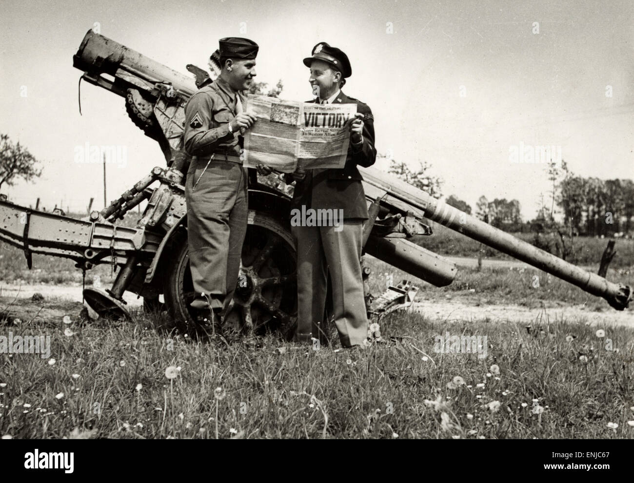 Victory in Europe. Soldiers read of victory, standing by a German 88 mm gun at Verdun, France on VE Day 1945 Stock Photo
