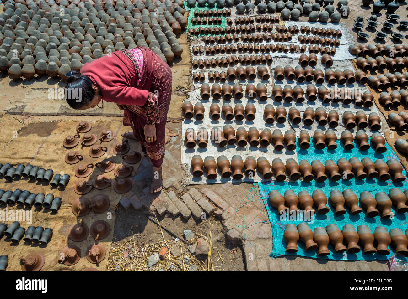 Bhaktapur, Nepal - 20 march 2015: Elderly woman placing potteries to dry on Pottery Square. Stock Photo