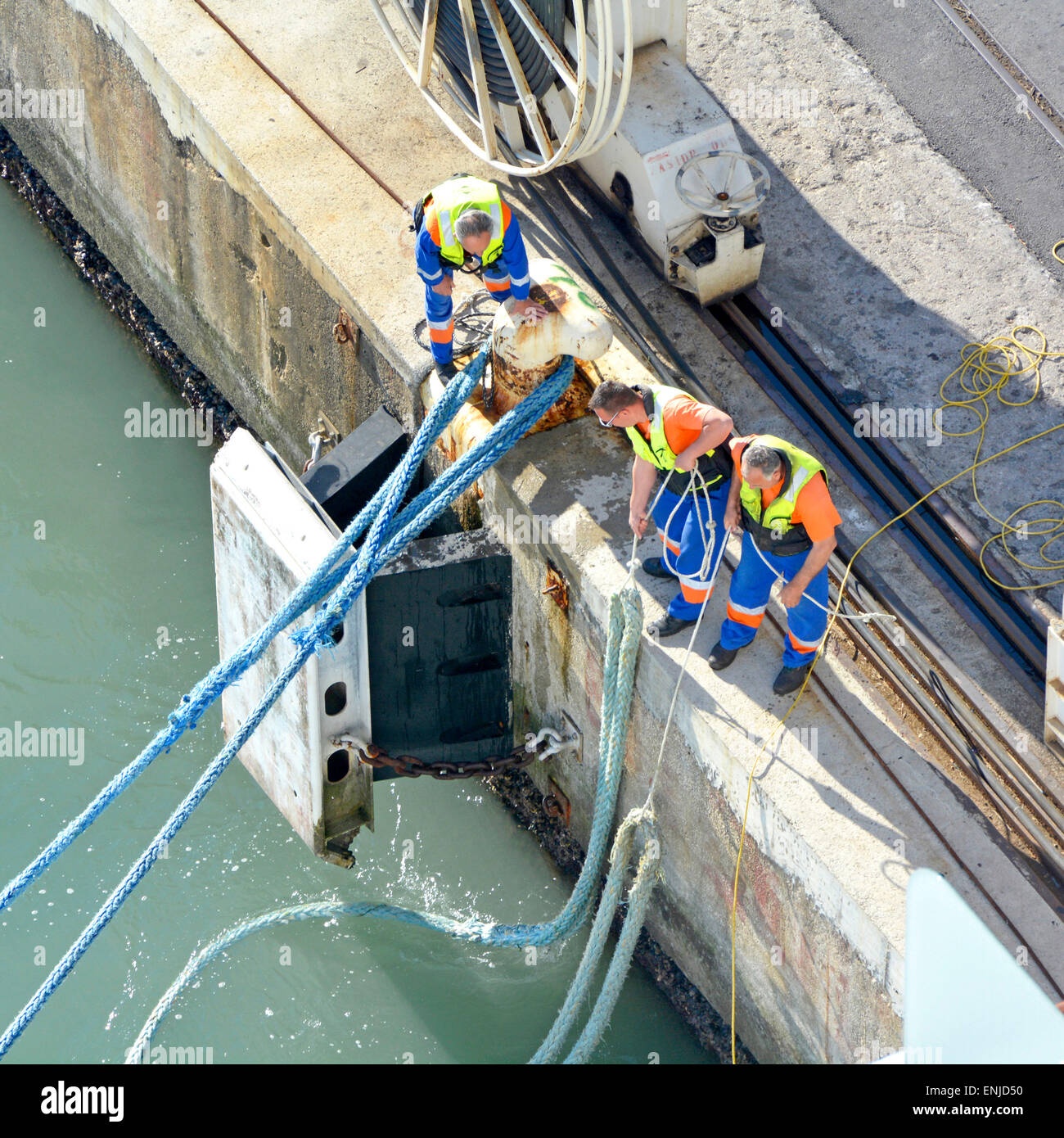Three dock hands manhandling heavy wet mooring ropes to secure big