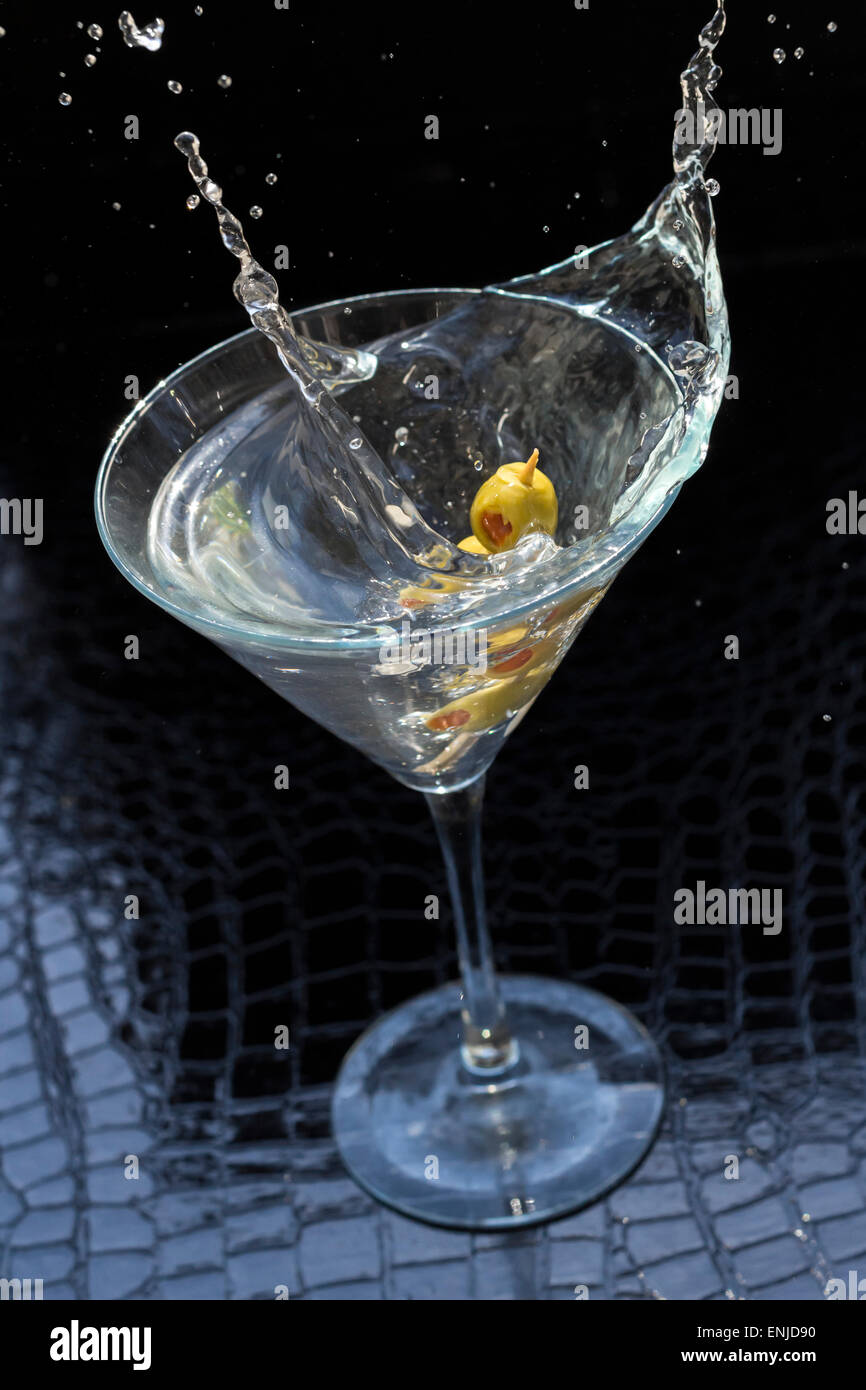 Splashing dirty martini garnished with green olives on toothpick Stock