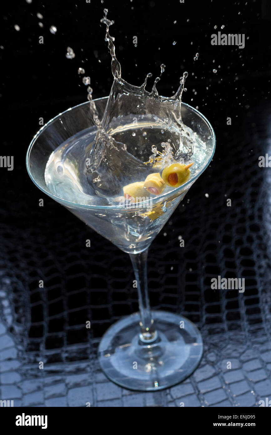 Splashing dirty martini garnished with green olives on toothpick Stock Photo