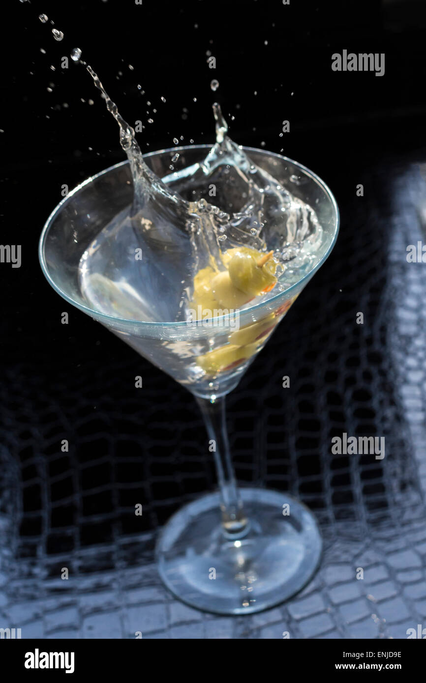 Splashing dirty martini garnished with green olives on toothpick Stock Photo