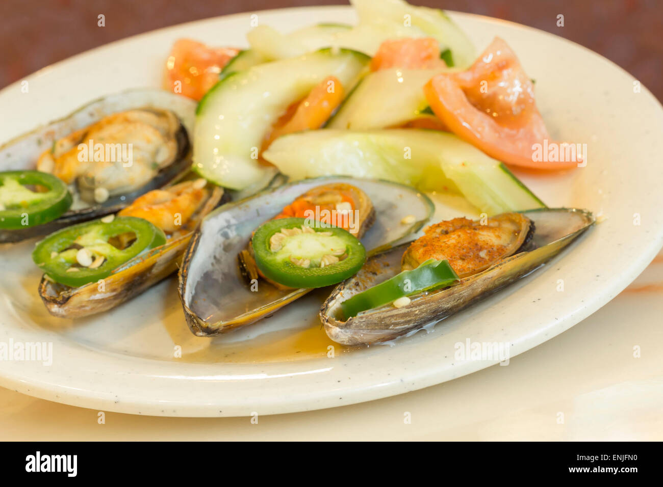 Spicy chili mussels with jalapeno slices and cucumber tomato salad Stock Photo