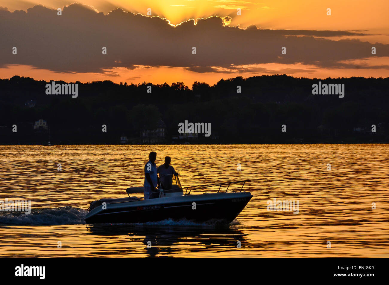 picturesque sunset over Lake Starnberg near Schloss Berg with the silhouette of a motorboat and the reflexion of the sun Stock Photo