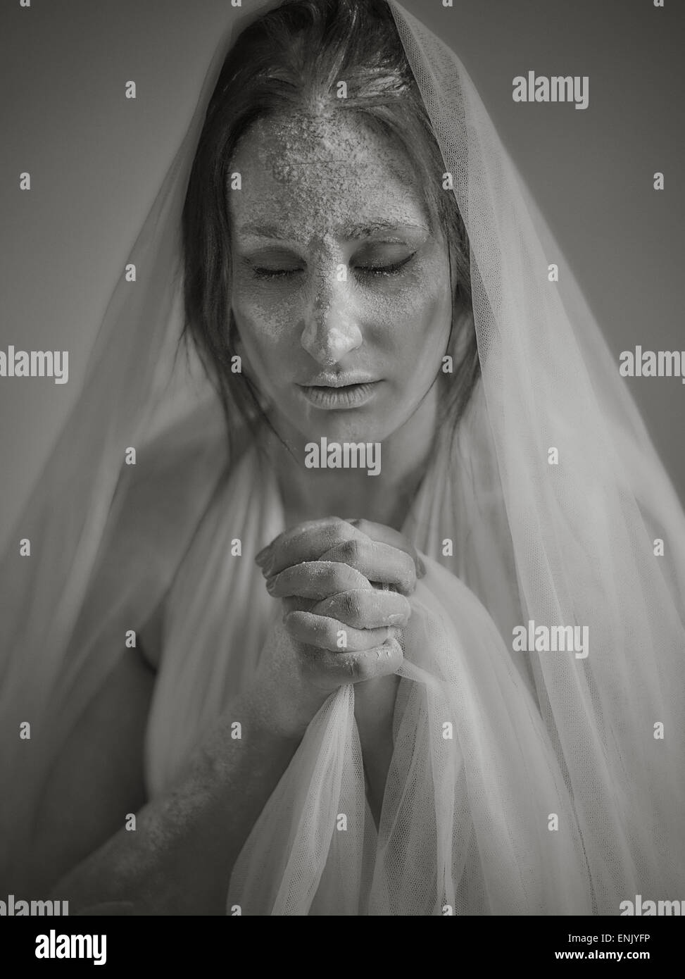 Close up woman face and ashes, she wearing white canvas and she praying, tinted black and white image, intentional noise added Stock Photo