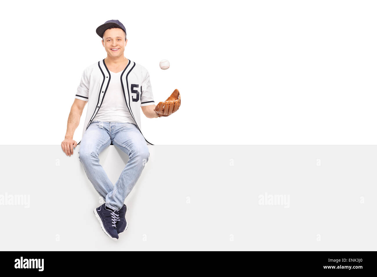 Young man playing with a baseball seated on a blank signboard and looking at the camera isolated on white background Stock Photo