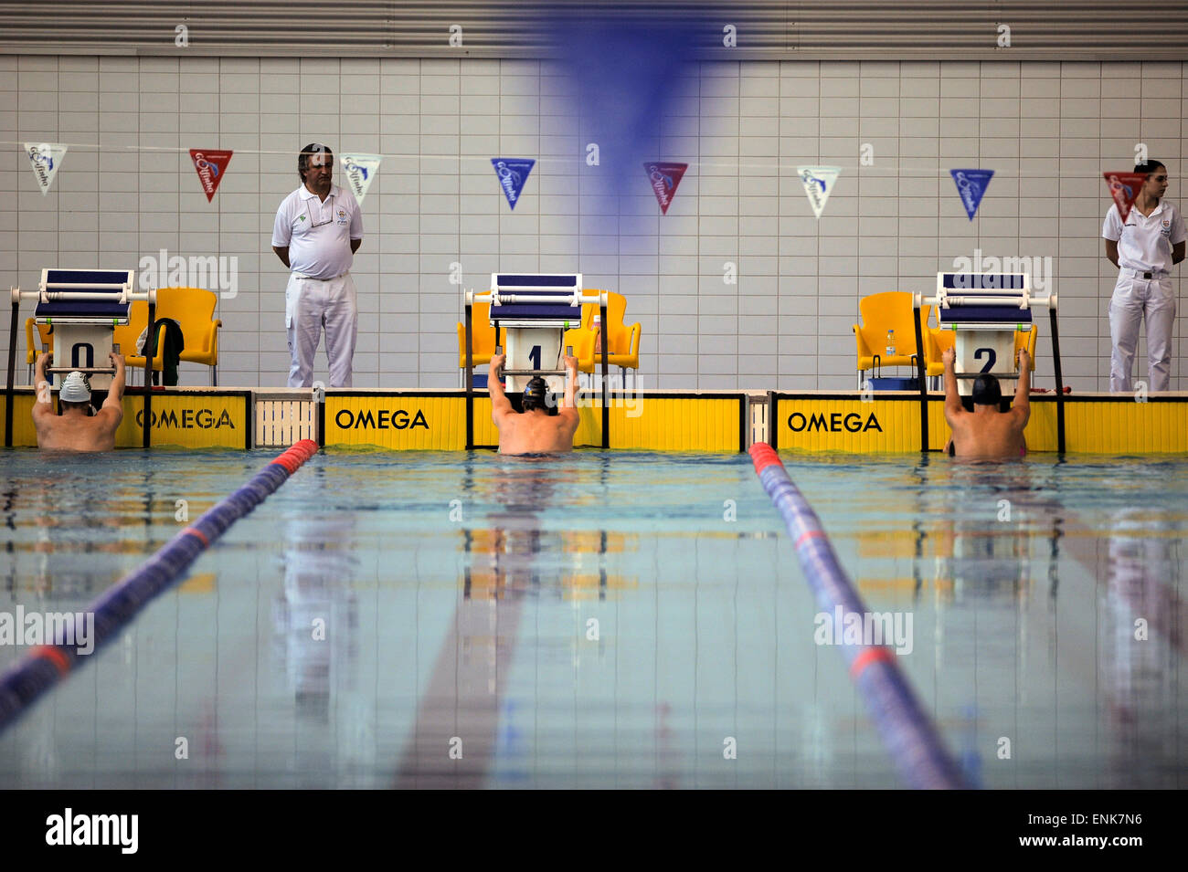 Athletes holding on to swimming pool's starting blocks getting ready to start backstroke swimming race during a competition meet Stock Photo