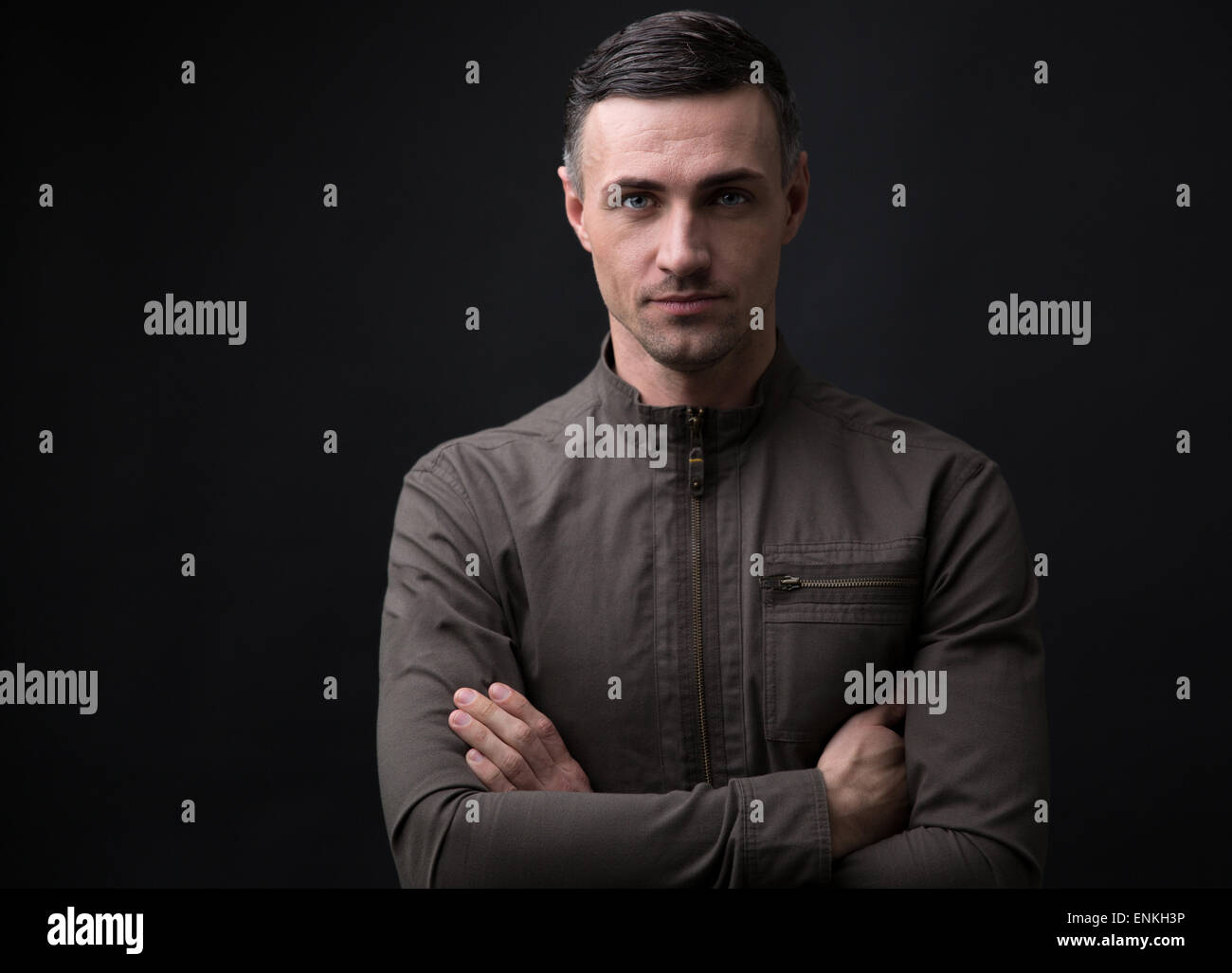 Portrait of a happy man standing with arms folded over black background ...