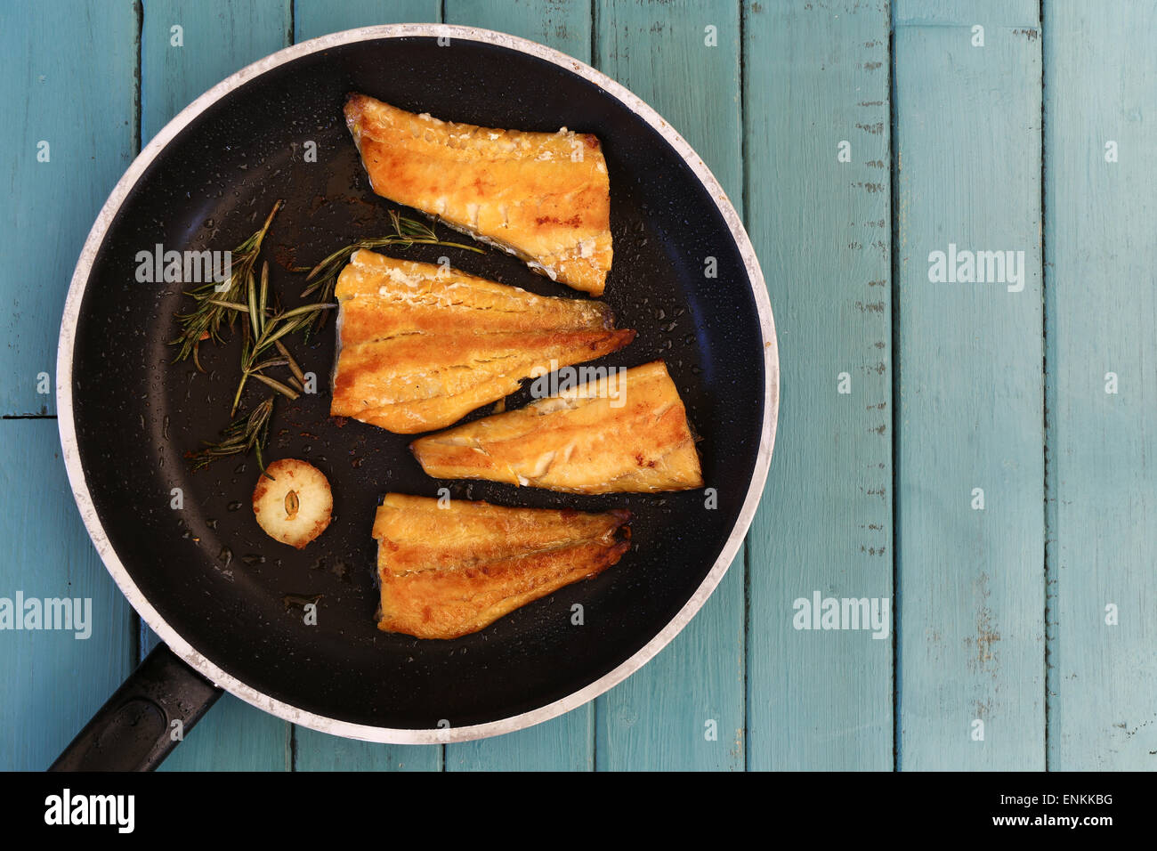 Four grilled smoked haddock fillets in cooking pan with rosemary brunch and garlic on turquoise