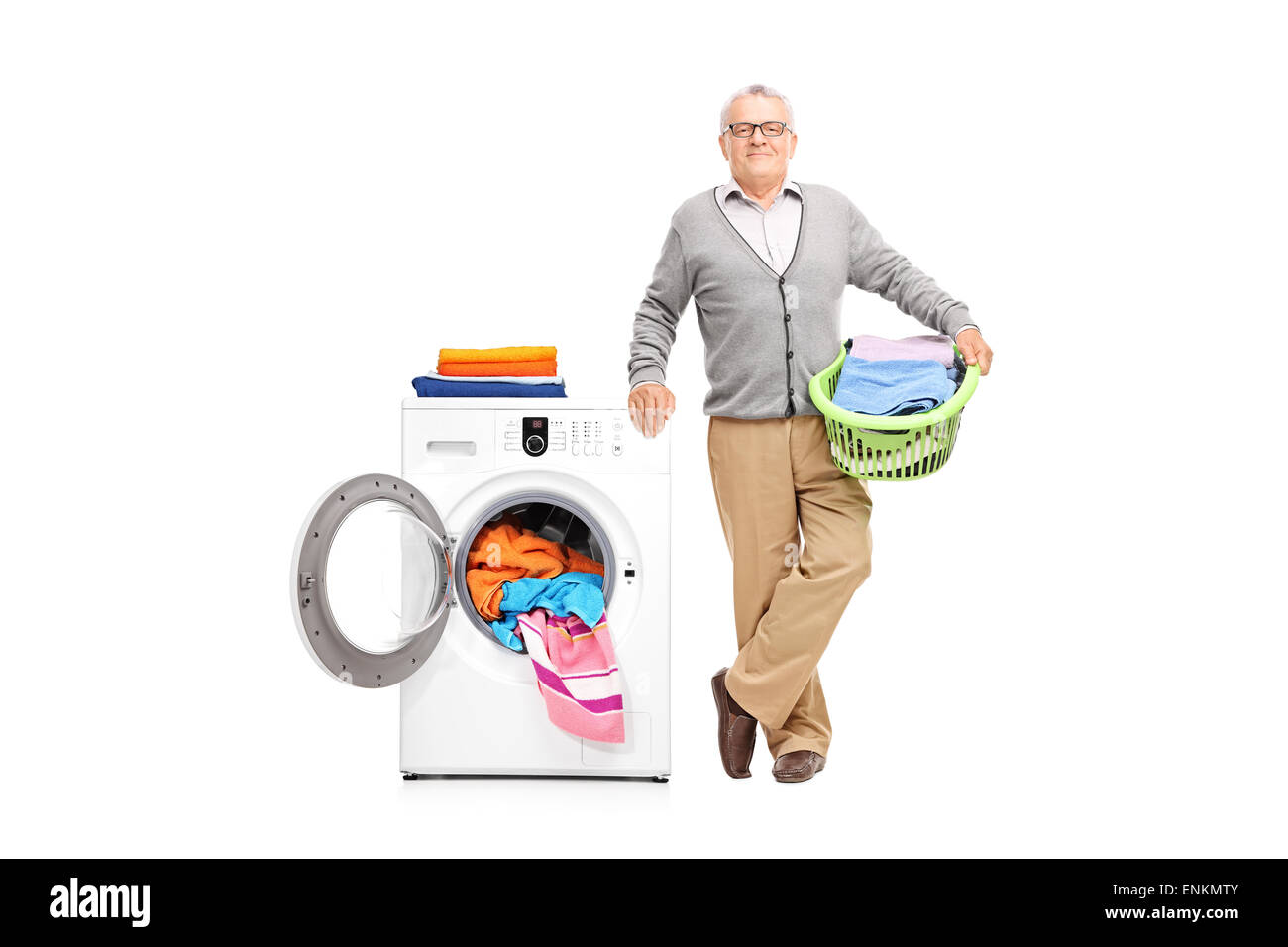 Senior gentleman holding a laundry basket full of clothes and posing next to a white washing machine Stock Photo