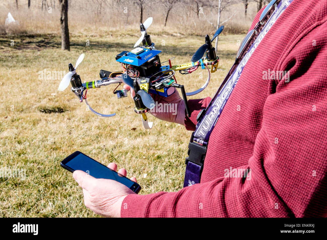 A 50 year old Caucasian man holds his Do It Yourself-built quadcopter drone,while looking at his mobile phone outdoors. USA. Stock Photo