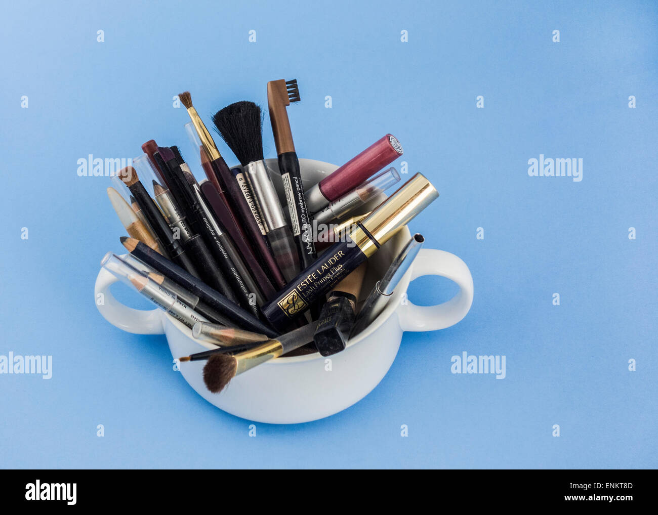 A cup holding many well-used applicator brushes and eye makeup. Isolated on blue. Stock Photo