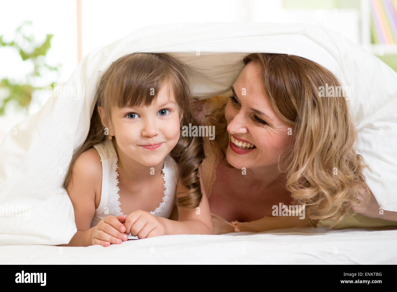 happy child and mother lying under blanket in bed together Stock Photo