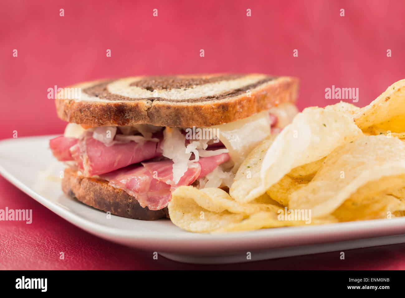 Classic reuben sandwich on pumpernickel swirl rye bread. A hearty meal with a side of pickle and chips Stock Photo