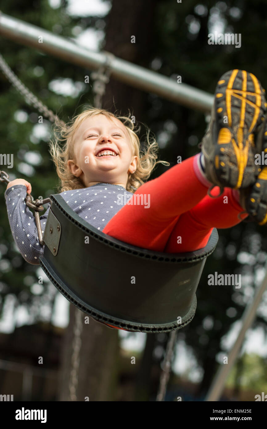 Elated toddler girl swinging high at playground in Portland, Oregon. Stock Photo
